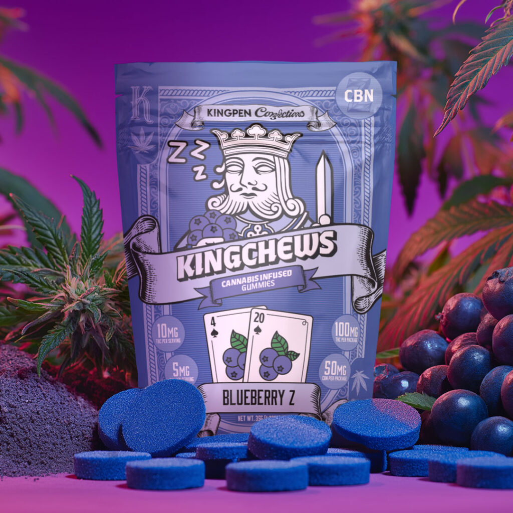Gummy package with sleeping playing card king holding blueberries and playing cards with numbers 4 and 20 with blueberries illustrated on cards. Gummy package is surrounded by gummies, real blueberries, flowering cannabis buds and leaves