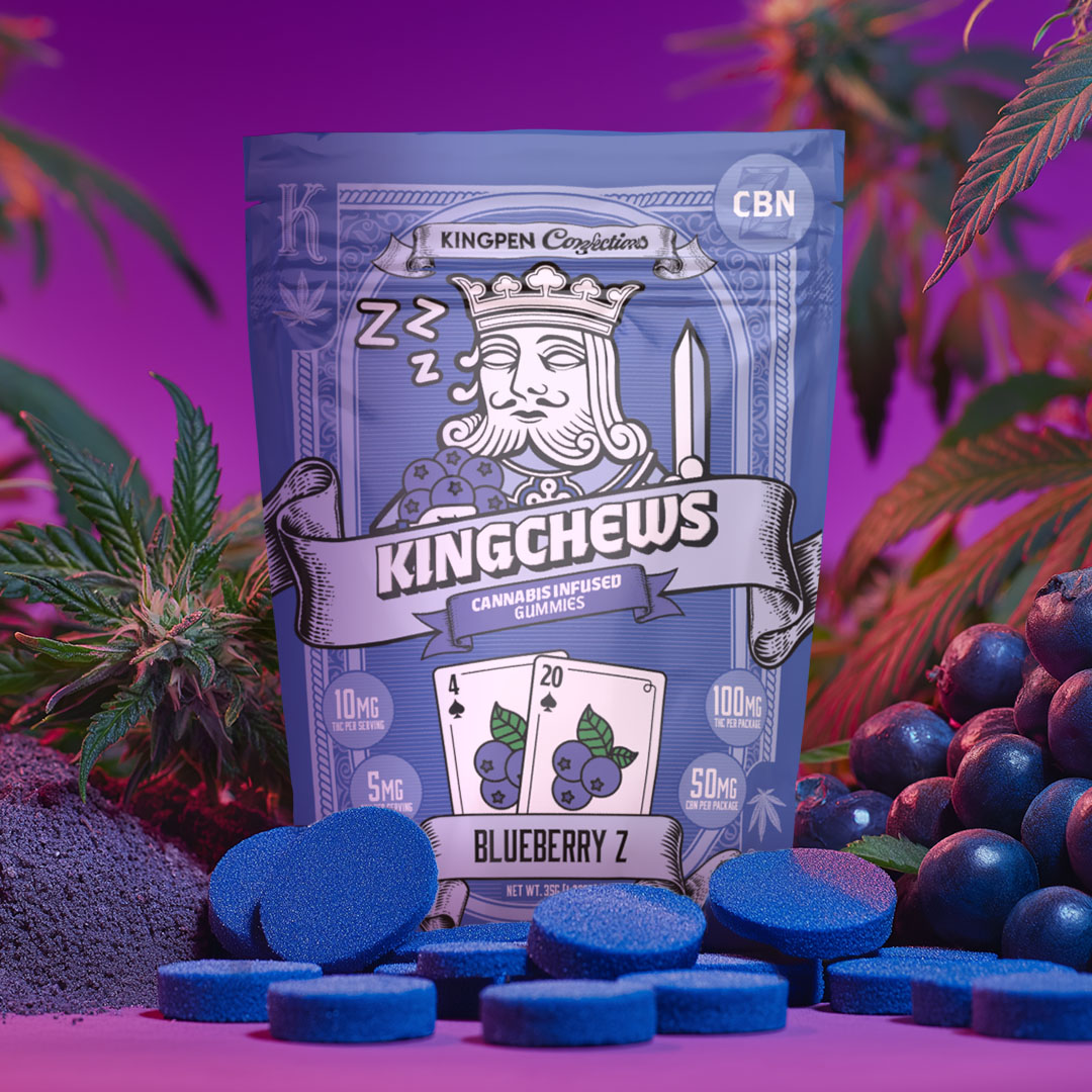 Gummy package with sleeping playing card king holding blueberries and playing cards with numbers 4 and 20 with blueberries illustrated on cards. Gummy package is surrounded by gummies, real blueberries, flowering cannabis buds and leaves