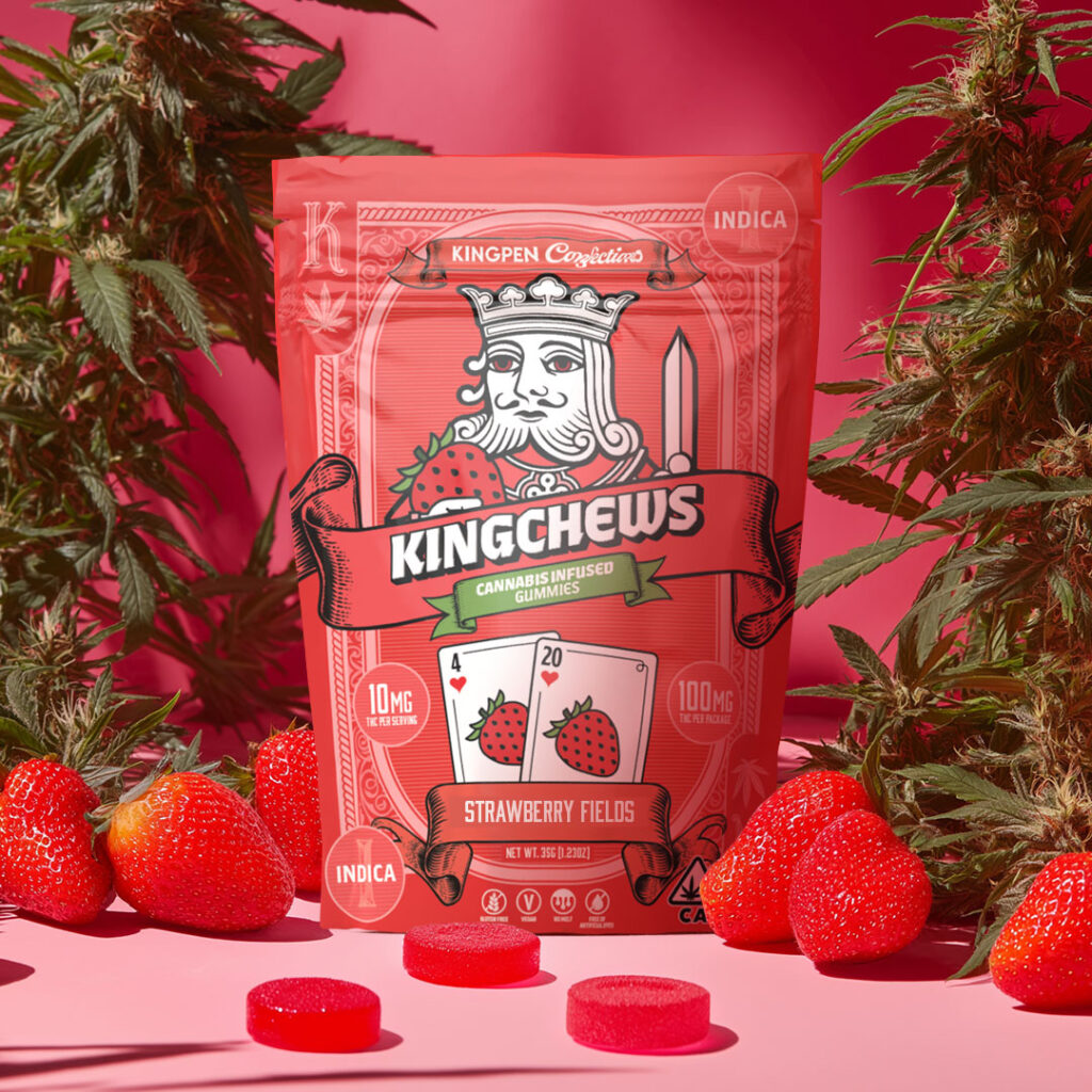 Gummy package with illustrated playing card king holding strawberry and playing cards with numbers 4 and 20 with blueberries illustrated on cards. Gummy package is surrounded by gummy tablets, real strawberries, flowering cannabis buds and leaves